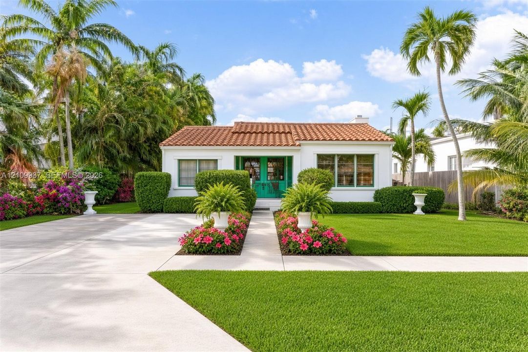 Single-story exterior featuring a clay tile roof, white stucco facade, manicured lawn, formal landscaping with flowering shrubs, and a concrete driveway
