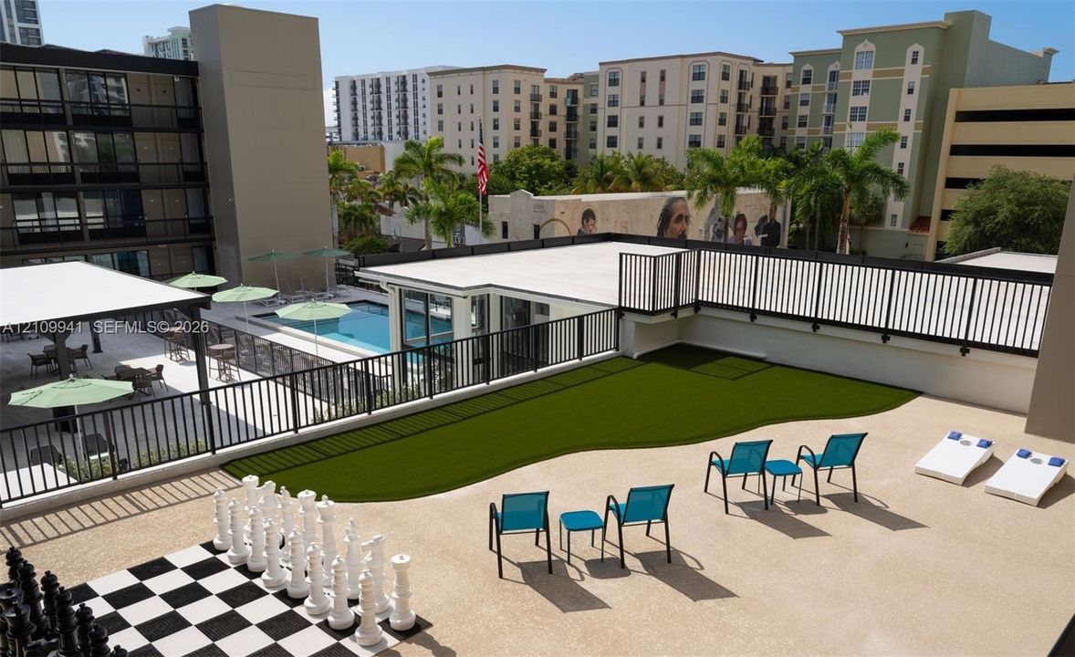 Elevated terrace featuring a synthetic grass lawn, oversized outdoor chess set, and black metal perimeter fencing