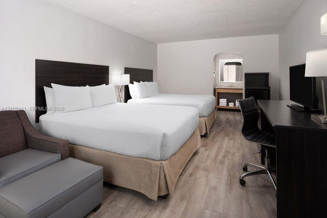 Wood-finish flooring, dark-toned wall-mounted headboards, and a built-in vanity area with a mirror