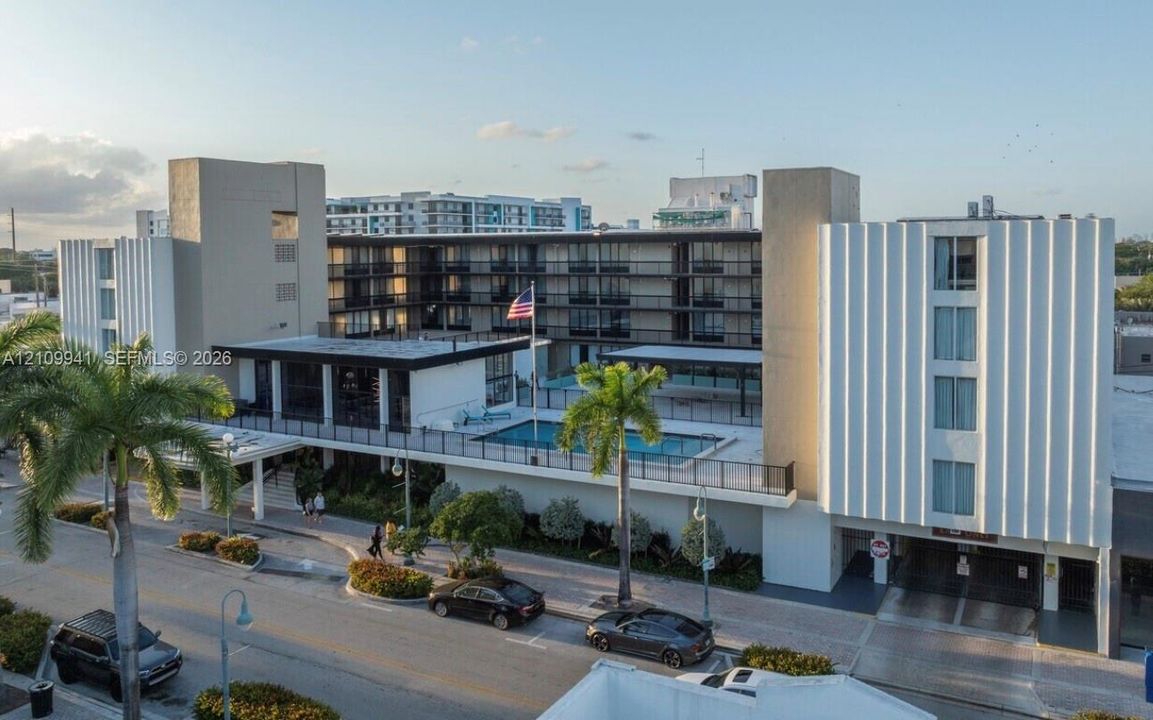 Mid-century modern architectural exterior featuring ribbed concrete facades, multi-story open-air corridors, an elevated swimming pool, and on-site parking