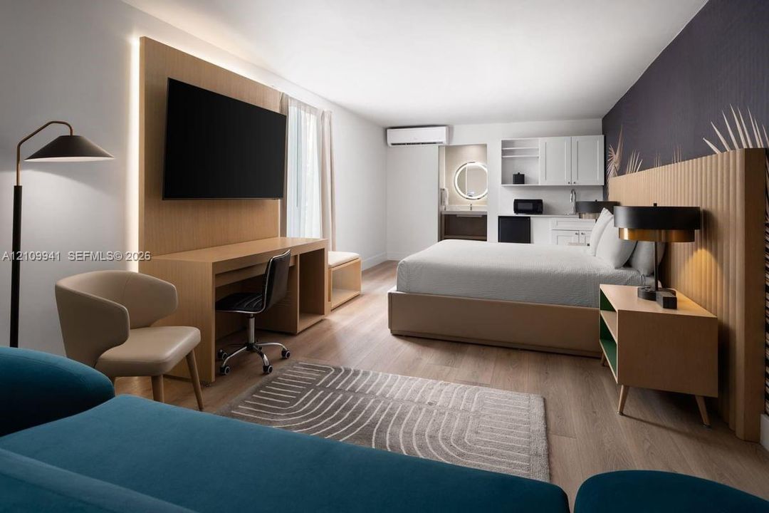 Wood-finish flooring, custom wood-paneled accent wall with integrated lighting, built-in desk, cabinetry with integrated kitchenette, and wall-mounted climate control unit