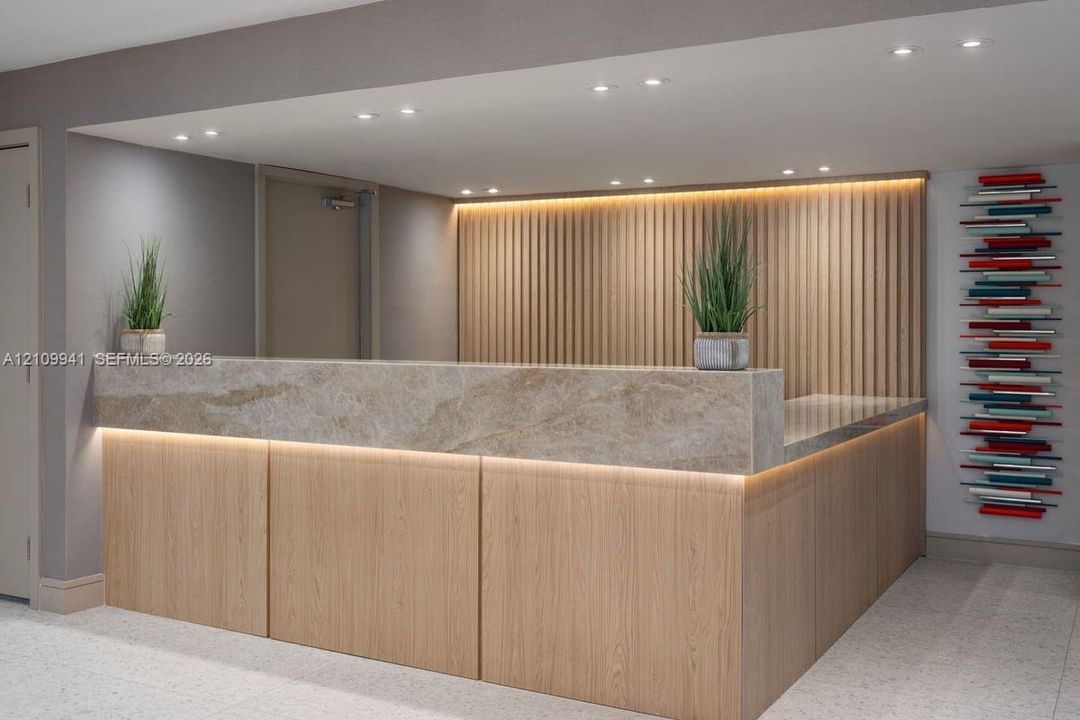 Reception desk featuring wood-paneled cabinetry, a stone-surfaced countertop, integrated under-counter lighting, and a vertical wood slat accent wall with recessed lighting