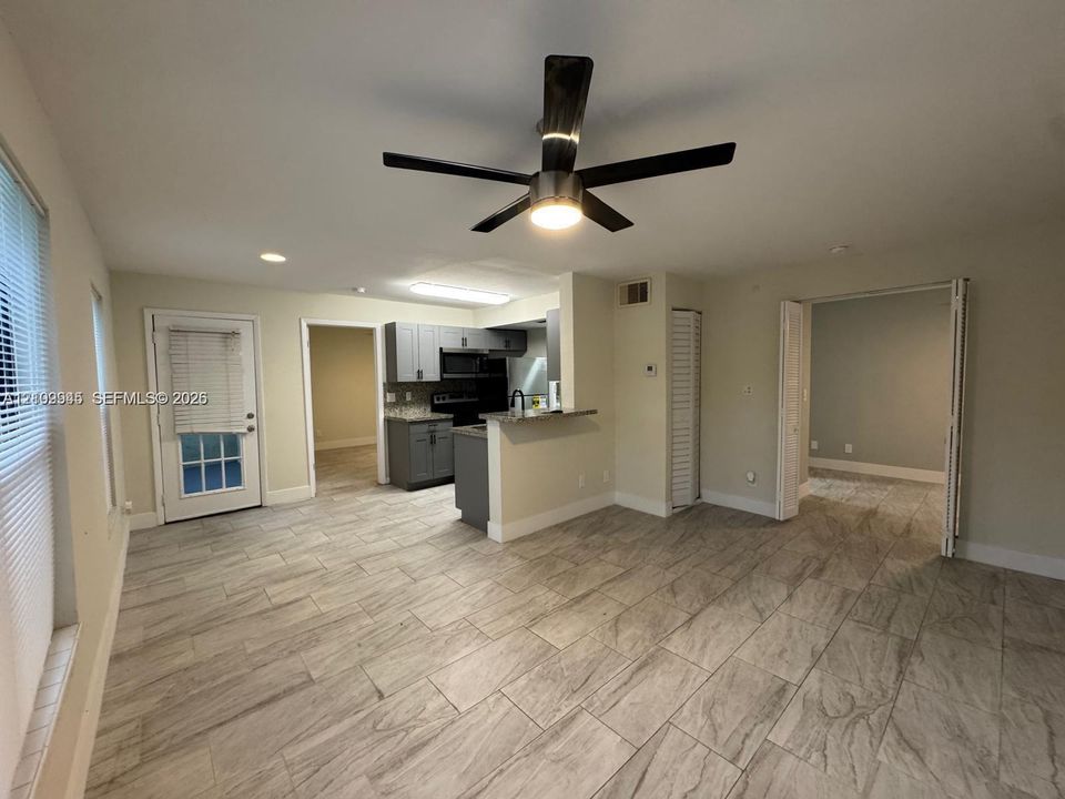 Interior space featuring large-format tile flooring, gray shaker-style cabinetry, an integrated breakfast bar, and a modern black ceiling fan with integrated lighting