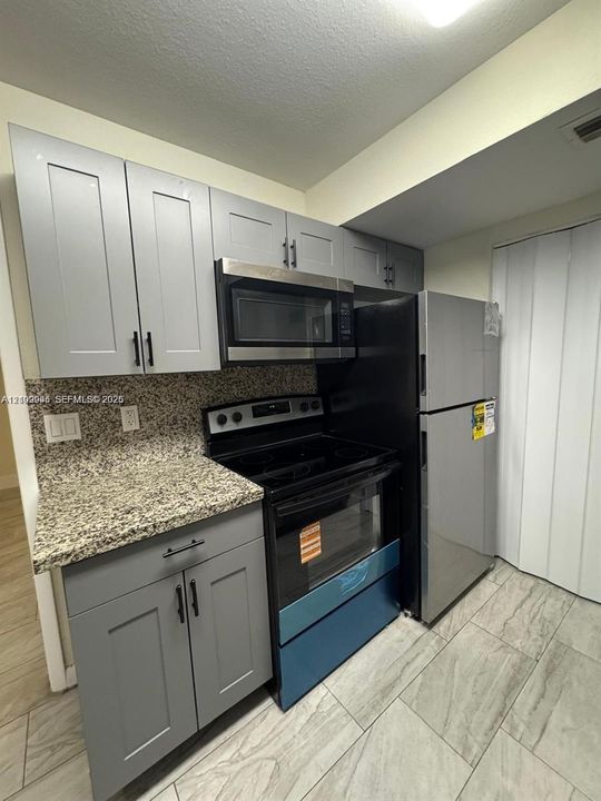Kitchen featuring grey shaker-style cabinetry, stone-finish countertops, stainless steel appliances, and tile flooring