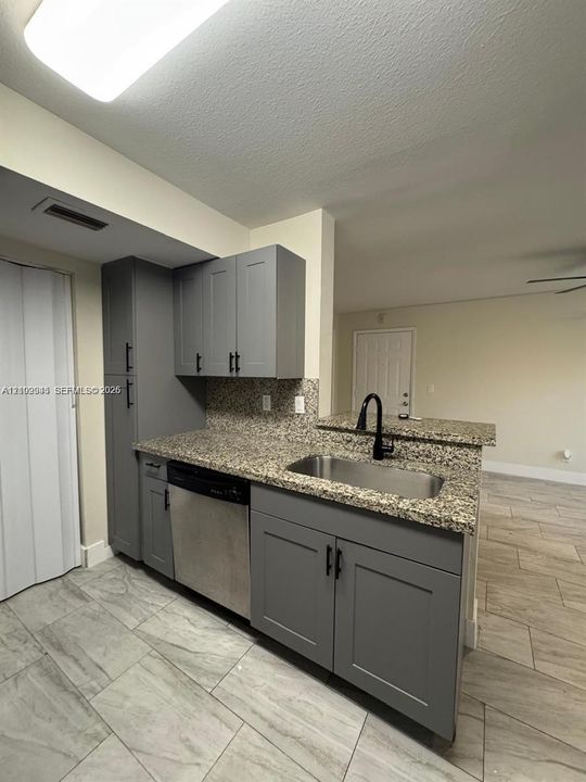 Kitchen featuring slate-grey shaker cabinetry, stone-finish countertops, stainless steel undermount sink with a matte black arched faucet, integrated dishwasher, and tile flooring