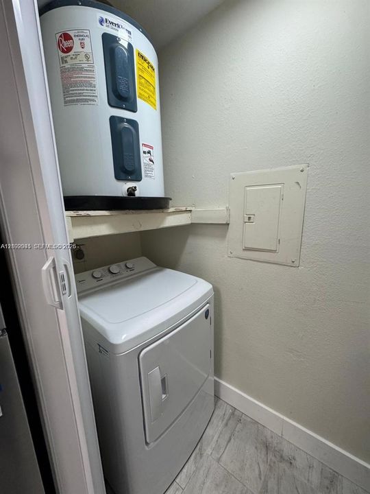 Utility closet featuring a water heater, built-in shelving, a dedicated electrical panel, and light-toned tile flooring