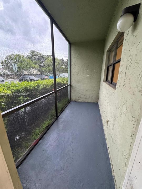 Screened-in balcony with painted concrete flooring, stucco exterior wall, and wall-mounted exterior light fixture