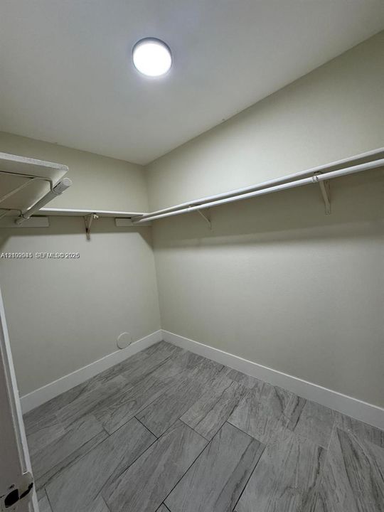 Walk-in closet featuring neutral wall finishes, grey wood-finish floor tiling, and tiered built-in shelving