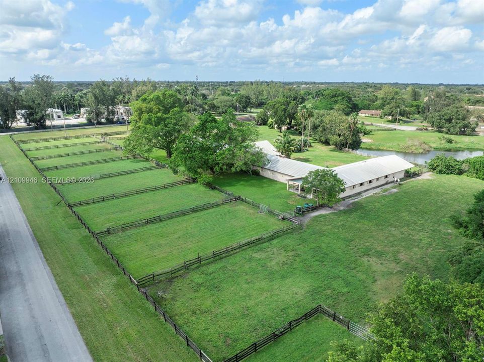 Expansive acreage featuring segmented pasture land, perimeter fencing, mature trees, and a pond