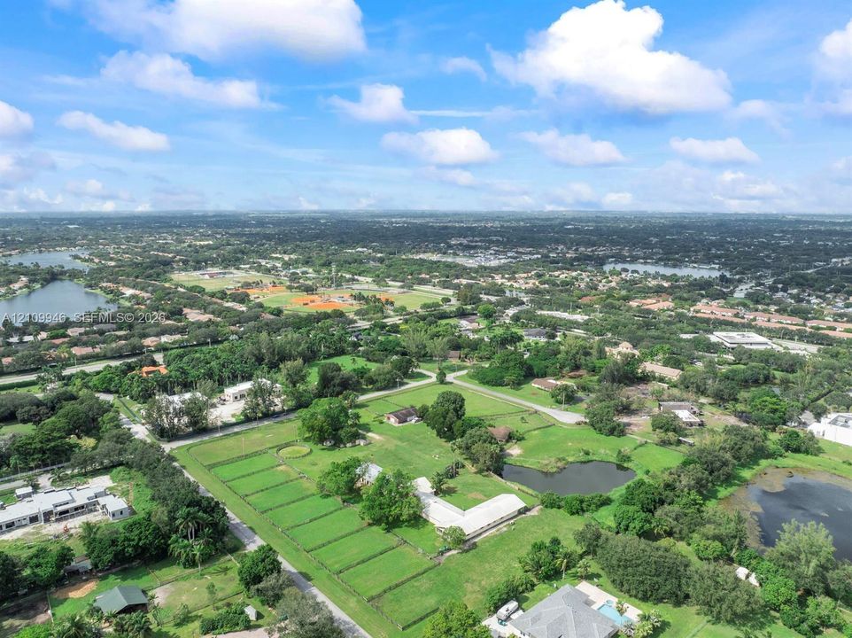 Aerial perspective of a sprawling property featuring fenced grazing pastures, mature trees, an on-site pond, and expansive green space
