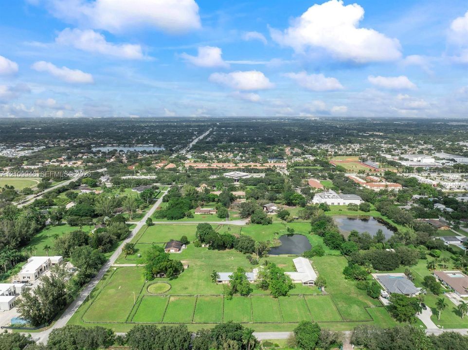 Aerial perspective of a sprawling property featuring extensive open green space, mature trees, and a private pond