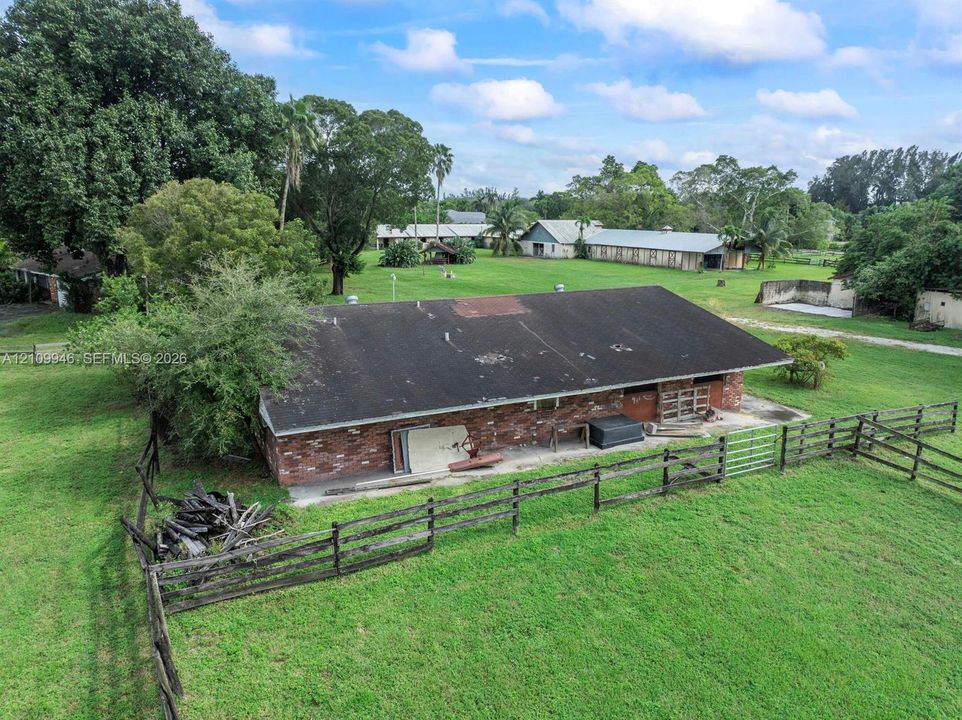 Expansive acreage featuring mature trees, post-and-rail wood fencing, and a multi-structure property layout with a central brick-exterior building