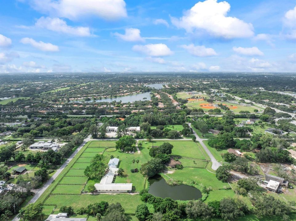 Aerial perspective of a sprawling property featuring expansive open acreage, fenced pastures, a private pond, and mature vegetation