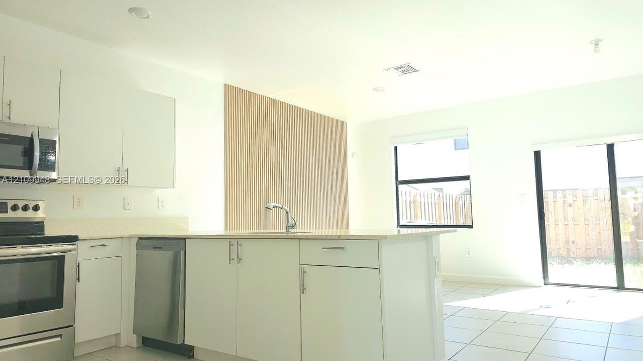 Kitchen featuring white cabinetry, stainless steel appliances, a central island with a sink, tile flooring, and a decorative wood-slat accent wall