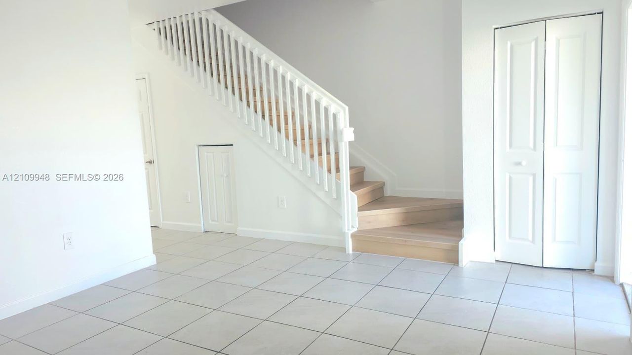 Staircase featuring wood-finish treads and a white balustrade, neutral tile flooring, and integrated bi-fold closet doors