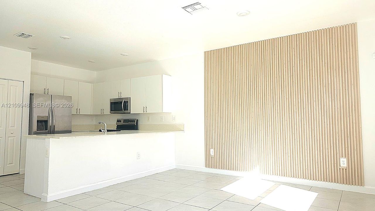 Kitchen featuring white cabinetry, stainless steel appliances, breakfast bar, tile flooring, and a decorative fluted wood-finish accent wall