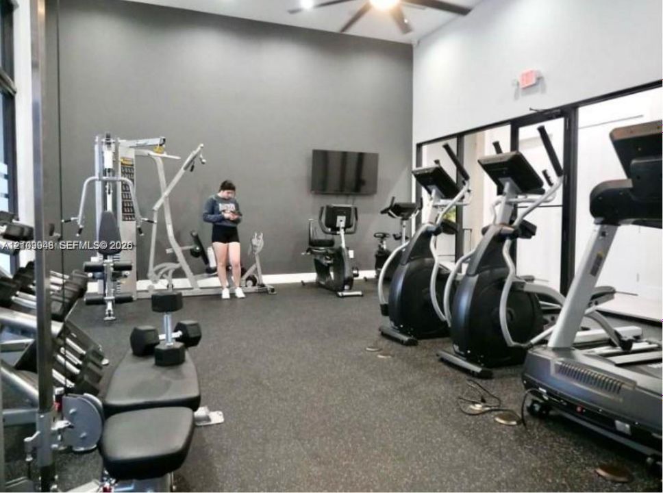 Fitness center featuring high ceilings, rubberized flooring, a wall-mounted television, and floor-to-ceiling glass paneling