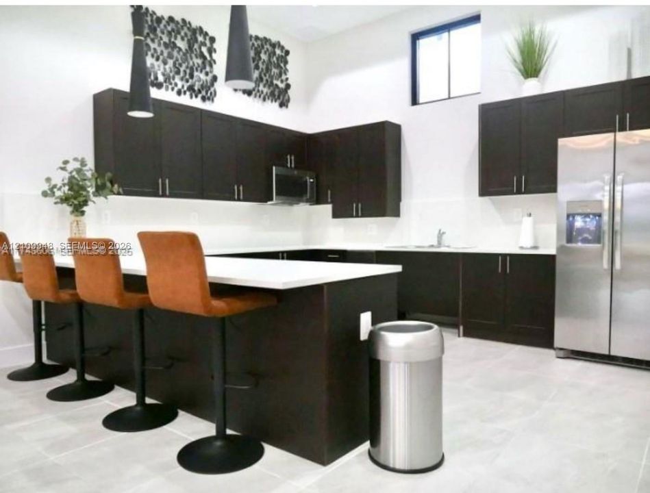 Kitchen featuring dark cabinetry, expansive white countertops, stainless steel refrigerator, built-in microwave, and pendant lighting