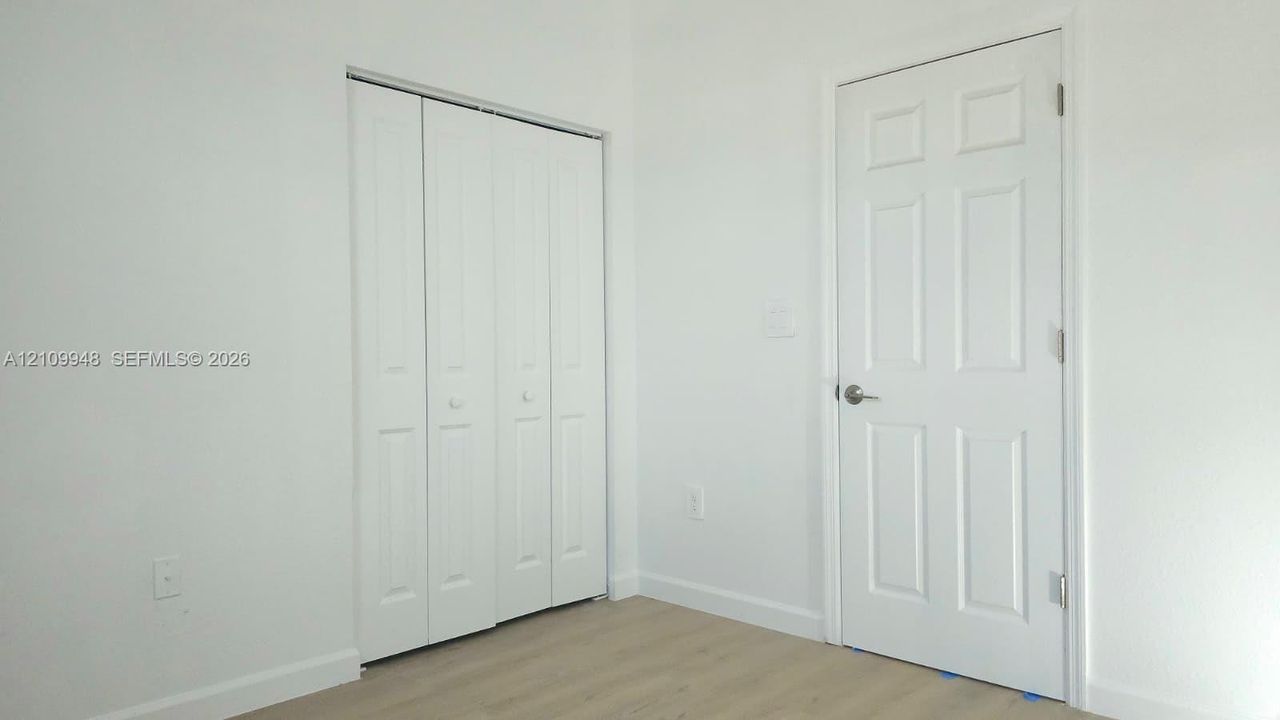 Wood-finish flooring, six-panel interior door, and white bi-fold closet doors