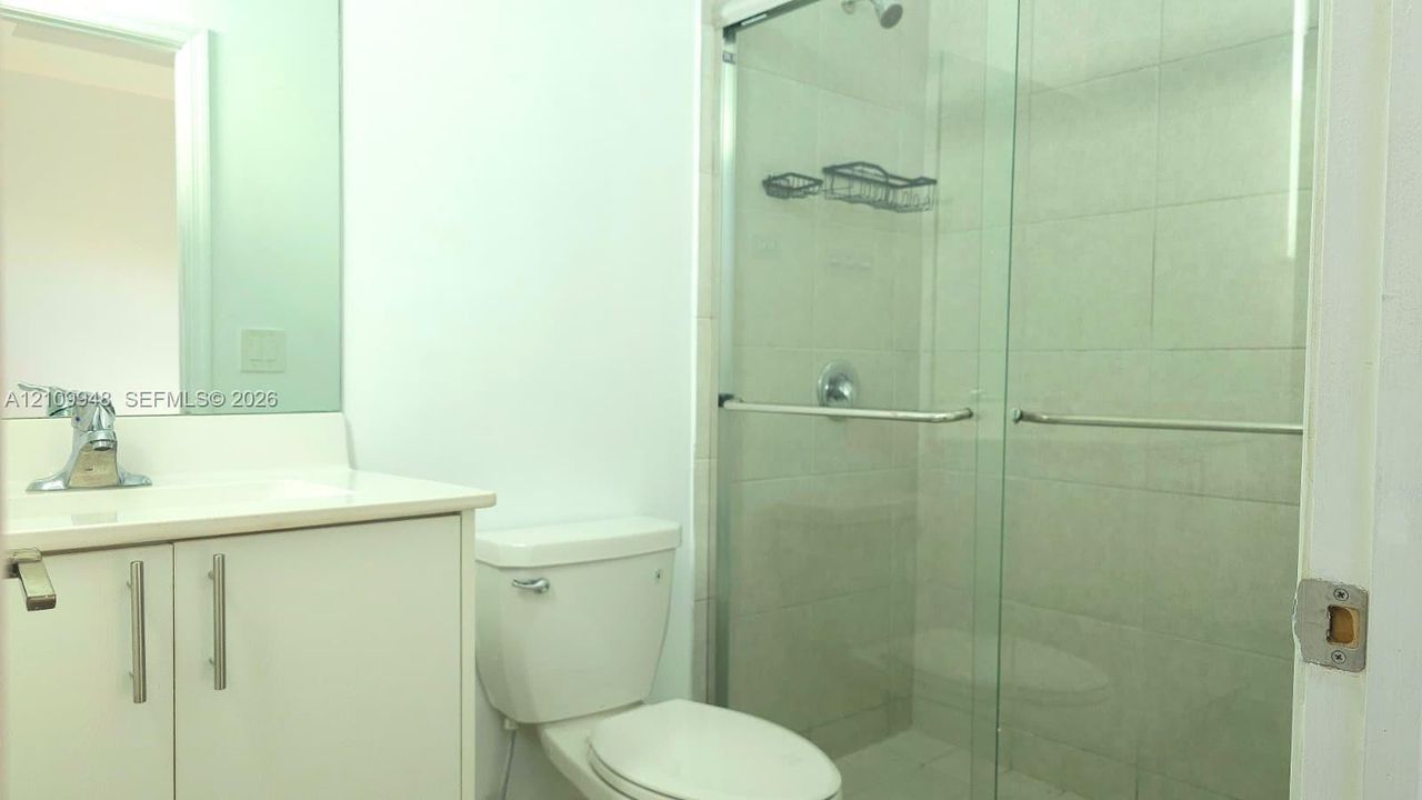Bathroom featuring a white vanity cabinet, rectangular under-mount sink with a polished chrome faucet, large wall-mounted mirror, and a walk-in shower with glass sliding doors and tile surround