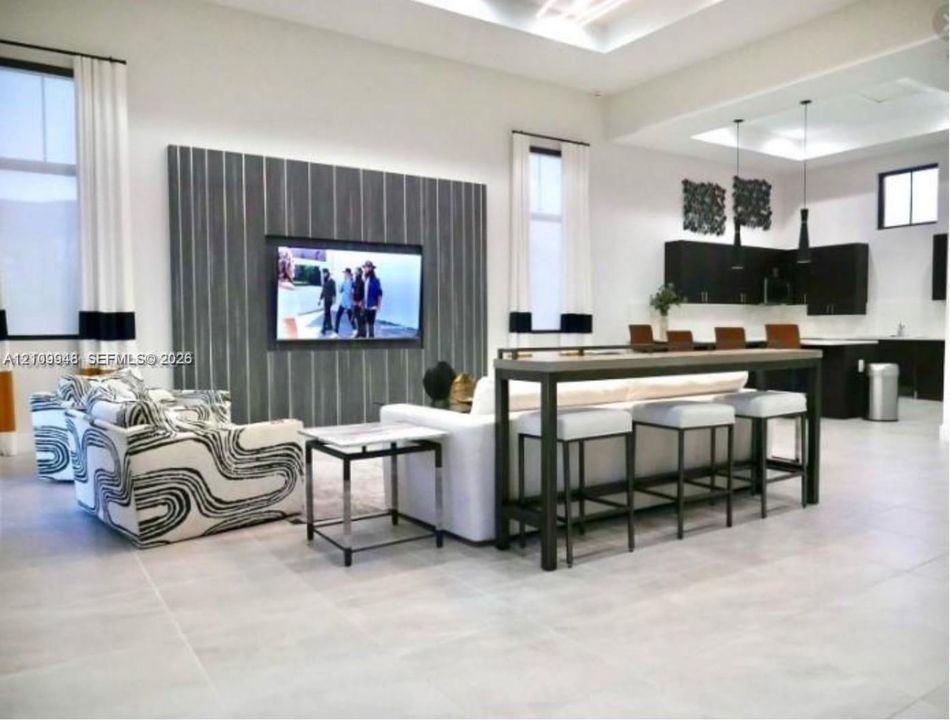 Open-concept living space featuring high ceilings with recessed lighting, large-format tile flooring, a floor-to-ceiling textured accent wall, and cabinetry with a dark finish