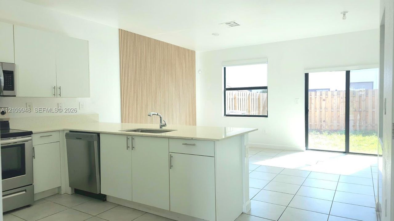 Kitchen featuring white cabinetry, solid surface countertops, stainless steel appliances, slatted wood-finish accent wall, and tile flooring