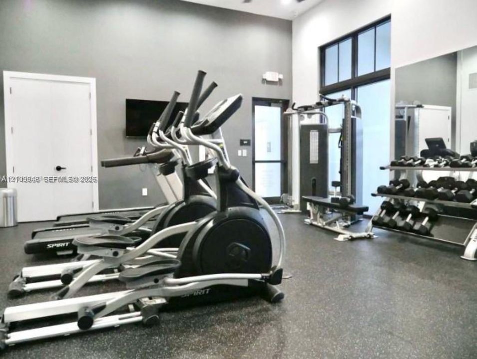 Fitness center featuring high ceilings, rubberized flooring, expansive wall mirrors, and large multi-pane windows