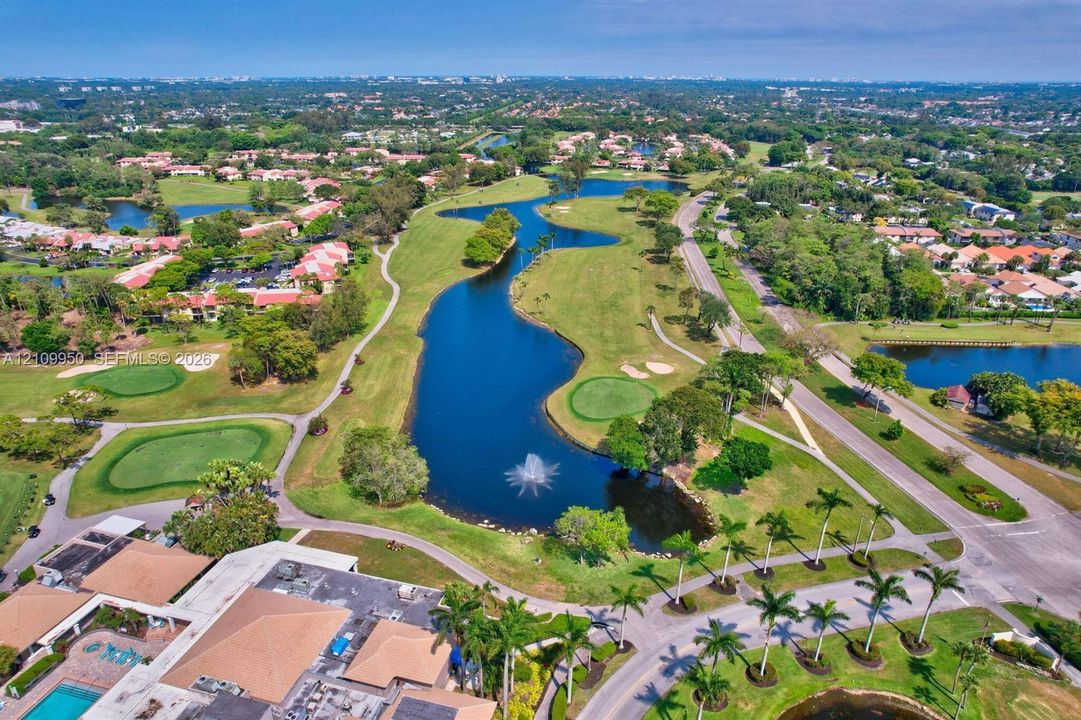 Aerial perspective of an expansive golf course featuring a winding waterway, a central fountain, manicured putting greens, and mature palm trees