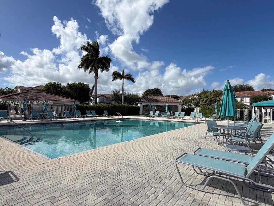 Swimming pool featuring a paved deck, metal handrails, and a covered pavilion