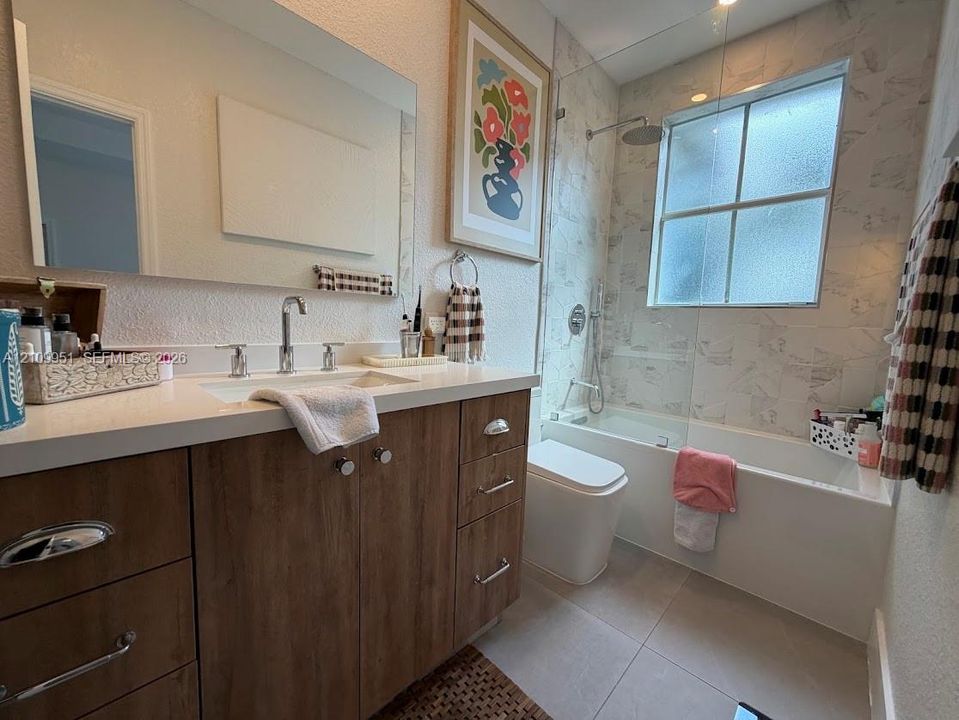 Bathroom featuring a wood-finish vanity with a stone countertop, an integrated sink with polished chrome fixtures, a frameless glass shower panel, and a tiled tub surround
