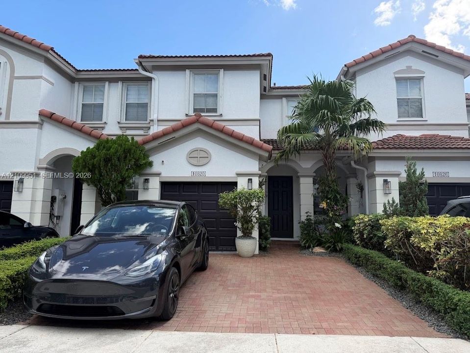Two-story stucco exterior featuring a terra cotta tile roof, arched entryway, brick-paver driveway, and a private garage