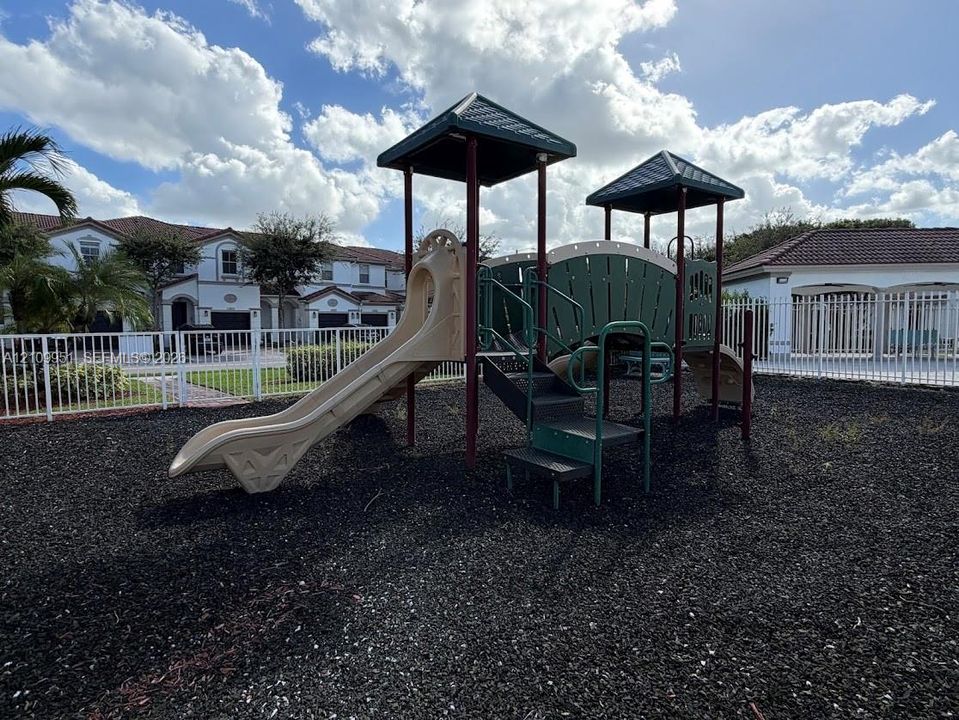 Outdoor recreation area featuring a multi-level structure with dual roof canopies, a slide, integrated stairs, and a surrounding protective fence