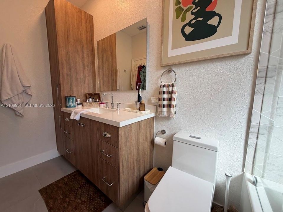 Wood-finish vanity cabinetry with integrated tall storage, solid surface countertop, rectangular undermount sink, and polished chrome faucet