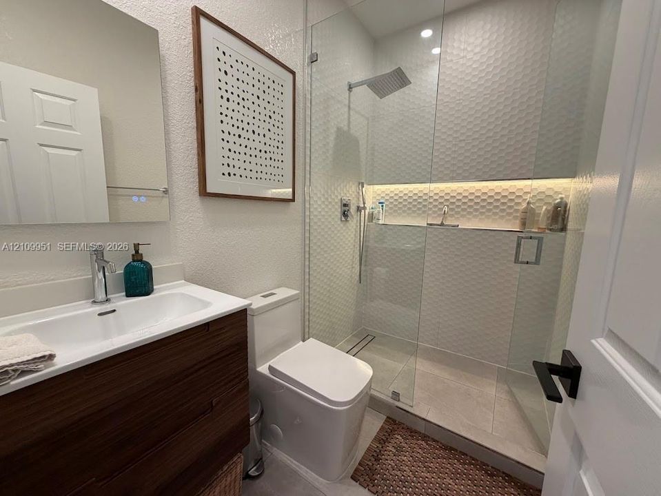 Bathroom featuring a wood-finish vanity with an integrated sink, frameless glass shower enclosure, textured hexagon wall tile, recessed shower lighting, and built-in shower niche