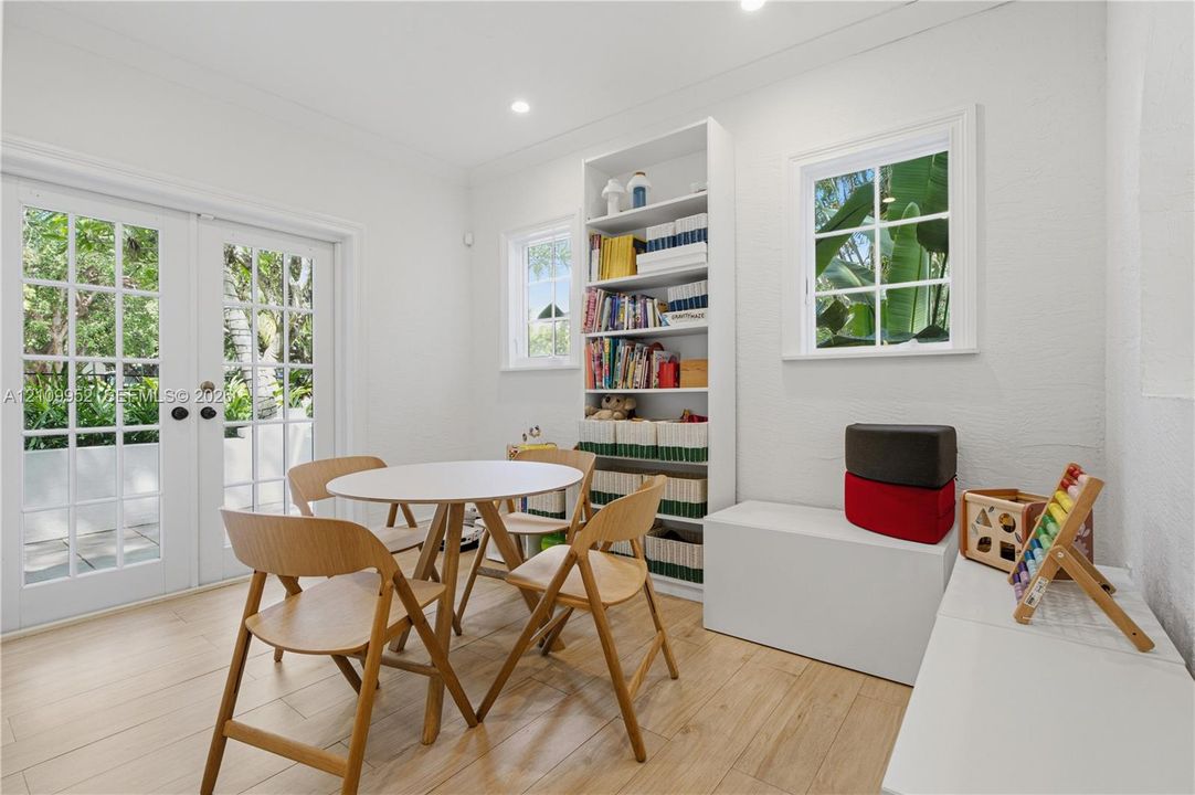 Room with wood-finish flooring, built-in floor-to-ceiling shelving, recessed lighting, and double glass-paneled doors