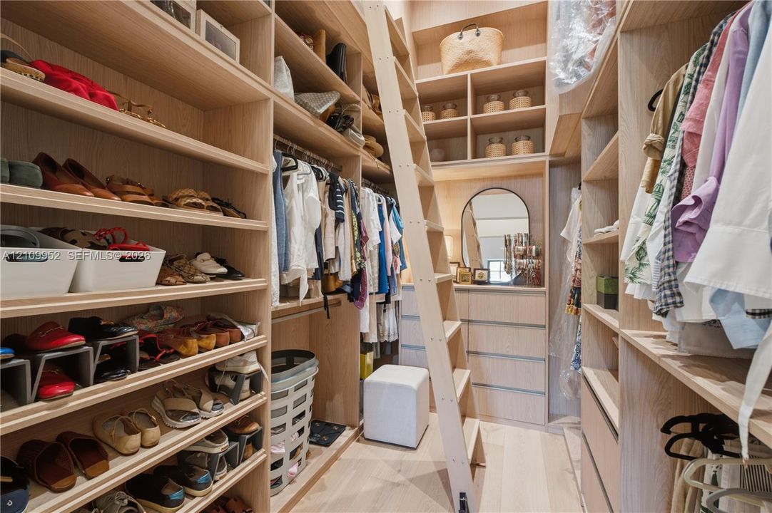 Custom light-toned wood cabinetry featuring extensive shelving, integrated clothing rods, built-in drawer units, and a sliding library-style ladder