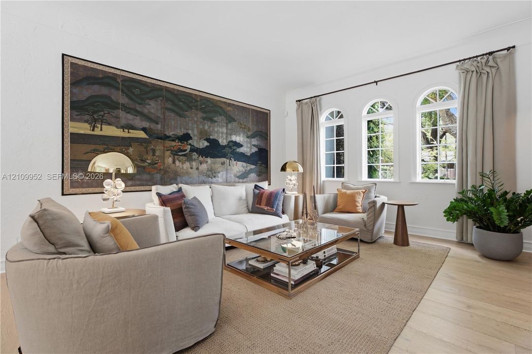 Living area featuring light-toned wood-finish flooring, three arched windows, and white walls