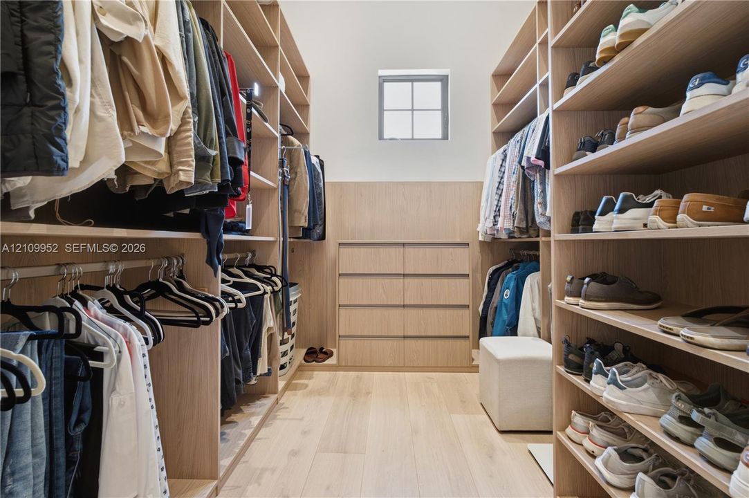 Custom walk-in closet featuring light-toned wood shelving, built-in dresser cabinetry, wood-finish flooring, and a window for natural light
