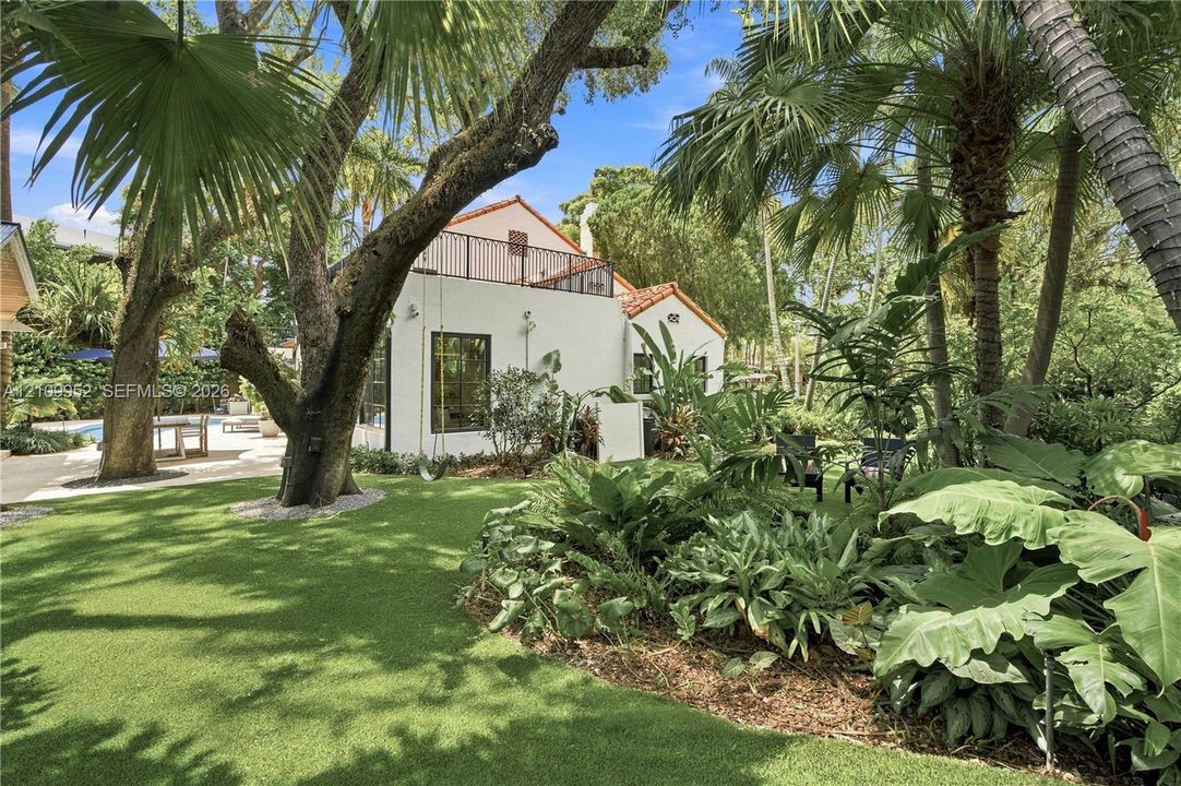 Exterior grounds featuring a stucco residence, clay tile roofing, a second-story metal railed balcony, mature palm trees, and expansive landscaping