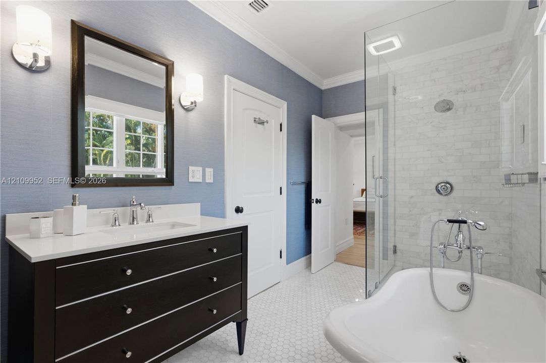 Bathroom featuring a vanity with a white countertop and rectangular sink, polished chrome fixtures, walk-in glass-enclosed shower with tiled surround, and a freestanding soaking tub