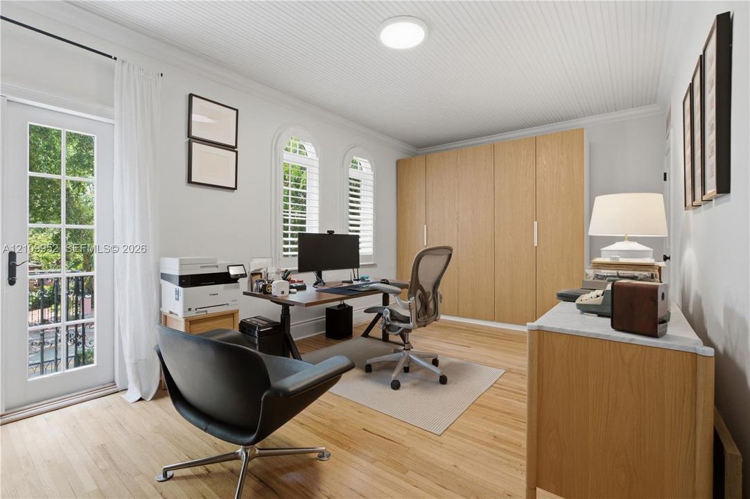 Beadboard ceiling, floor-to-ceiling built-in wood-finish cabinetry, arched windows with interior shutters, wood-finish flooring, and glass-paned exterior door
