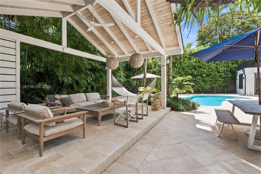 Covered outdoor patio featuring a vaulted tongue-and-groove ceiling, natural stone flooring, dual pendant lighting, and a swimming pool