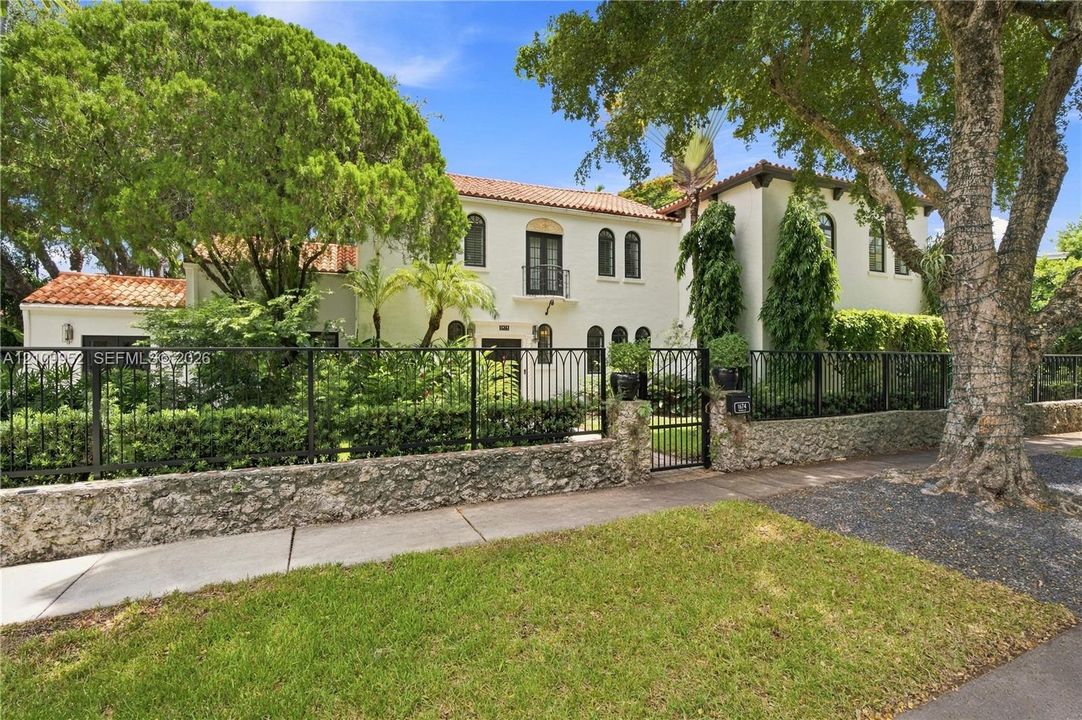 Mediterranean-style exterior featuring a clay tile roof, stucco facade, arched window detailing, and a stone-masonry perimeter wall with wrought-iron fencing