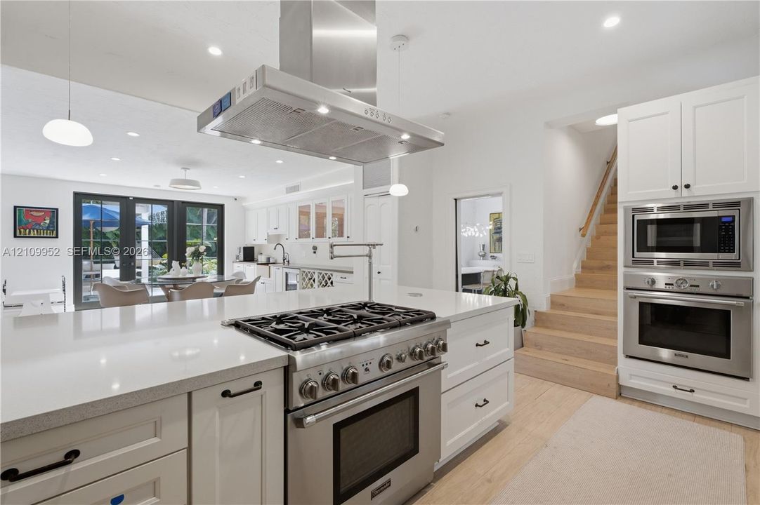 Kitchen featuring a large central island with quartz countertops, stainless steel professional-grade gas range, built-in double oven and microwave, custom white cabinetry, and light-tone wood-finish flooring