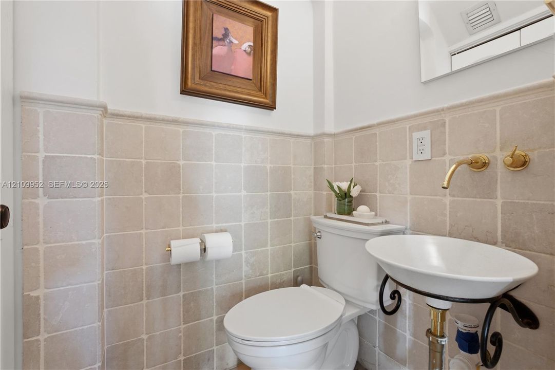 Wall-mounted wall-to-wall stone tile wainscoting, wall-mounted gold-tone faucet, and oval pedestal sink with ornate metal supports