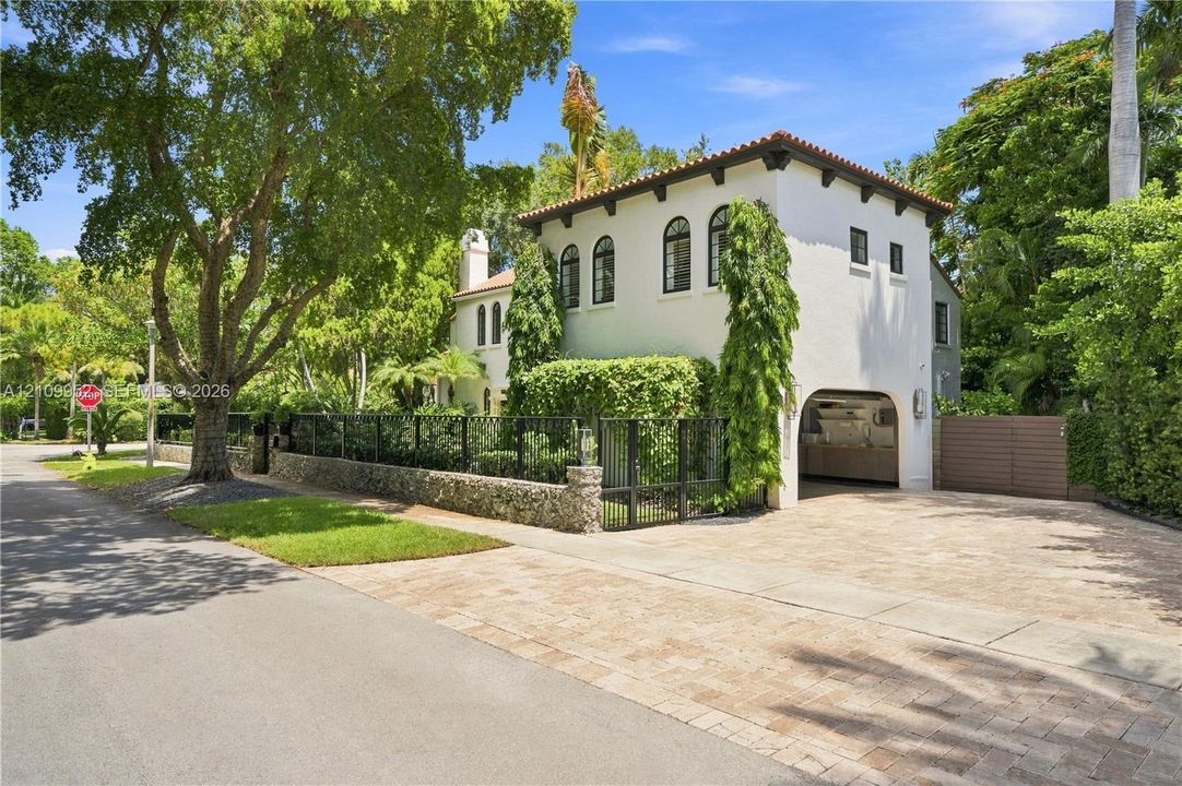 Stucco exterior featuring an arched entryway, tile roof, decorative corbels, stone masonry wall, and paved driveway