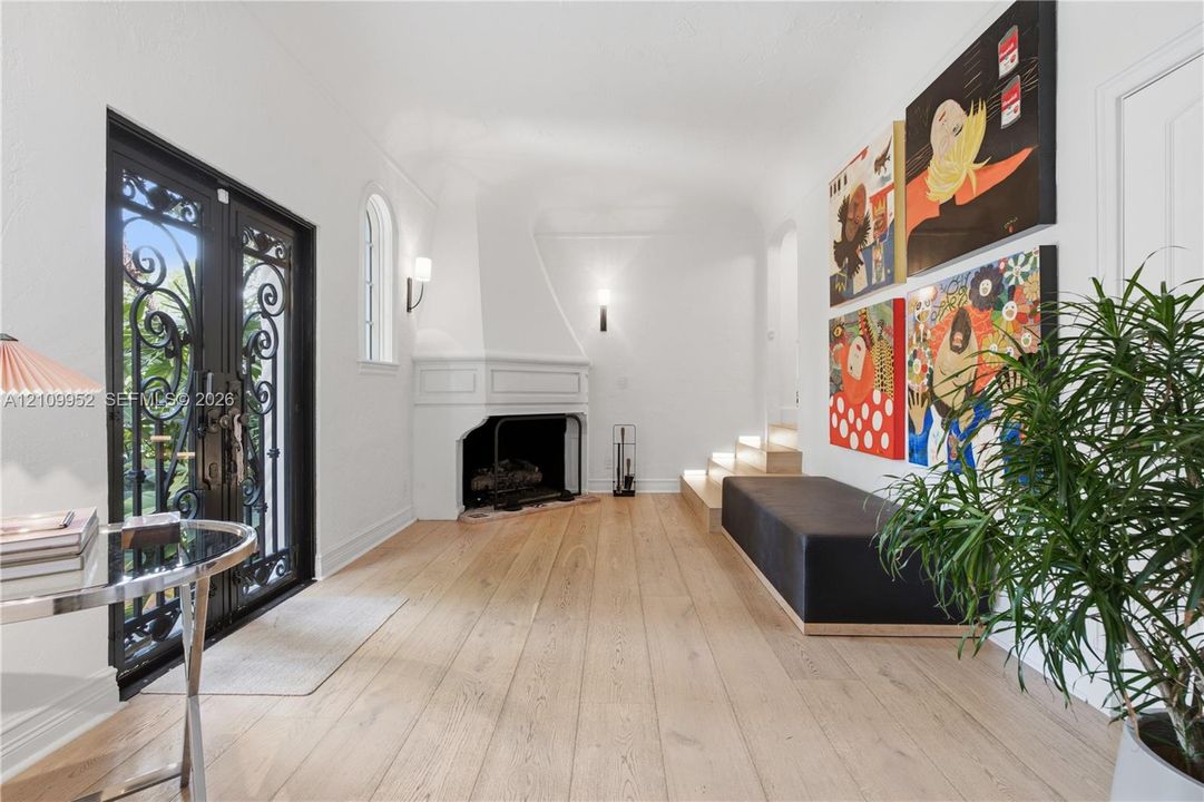 Entryway featuring double iron-grille doors, wood-finish flooring, a corner fireplace with a white mantel, and integrated step lighting