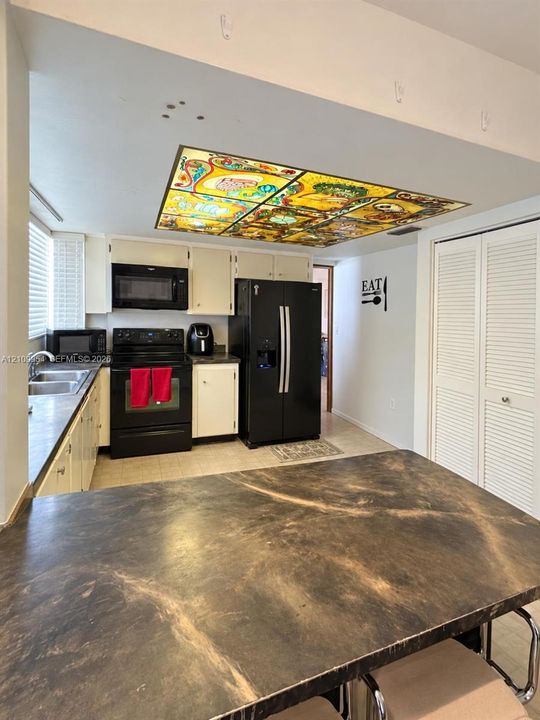 Kitchen featuring a decorative stained-glass ceiling fixture, dark-tone laminate countertops, solid-color cabinetry, black appliances, and louvered double-door storage