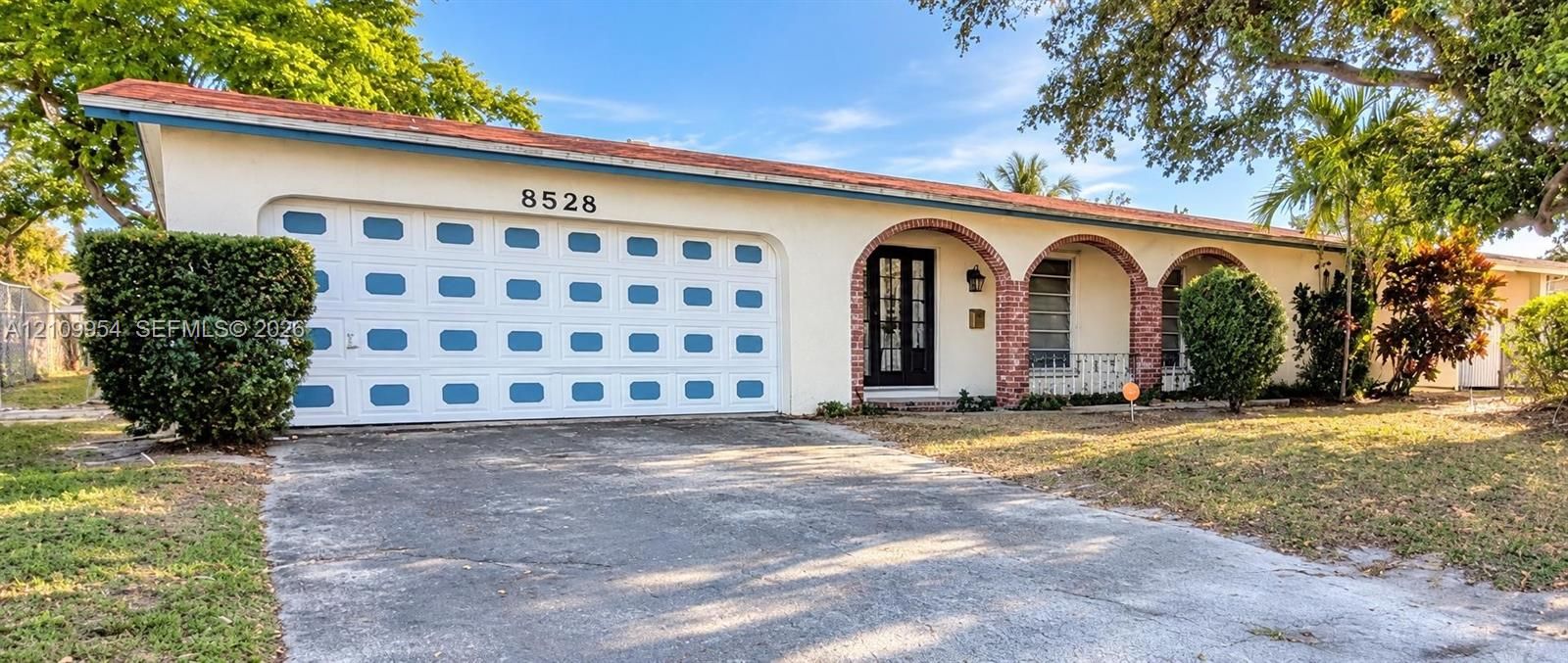 Single-story residence featuring a terracotta-tiled roof, white exterior, arched masonry entryway, multi-panel garage door, and metal window grilles