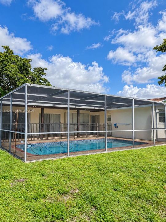 In-ground swimming pool enclosed by a screen lanai, featuring a concrete patio and open green space